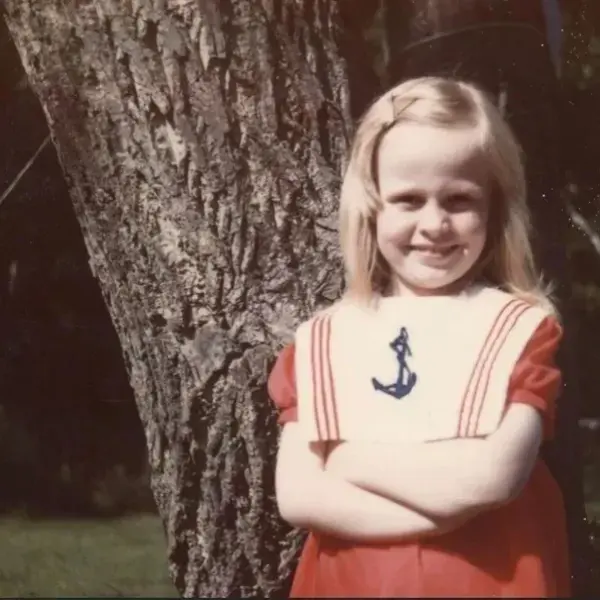 A young girl standing in front of a tree.